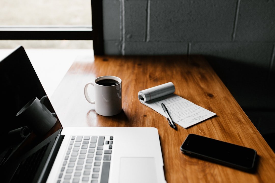 Escritorio de trabajo con una computadora portátil, un teléfono, una libreta y una taza de café